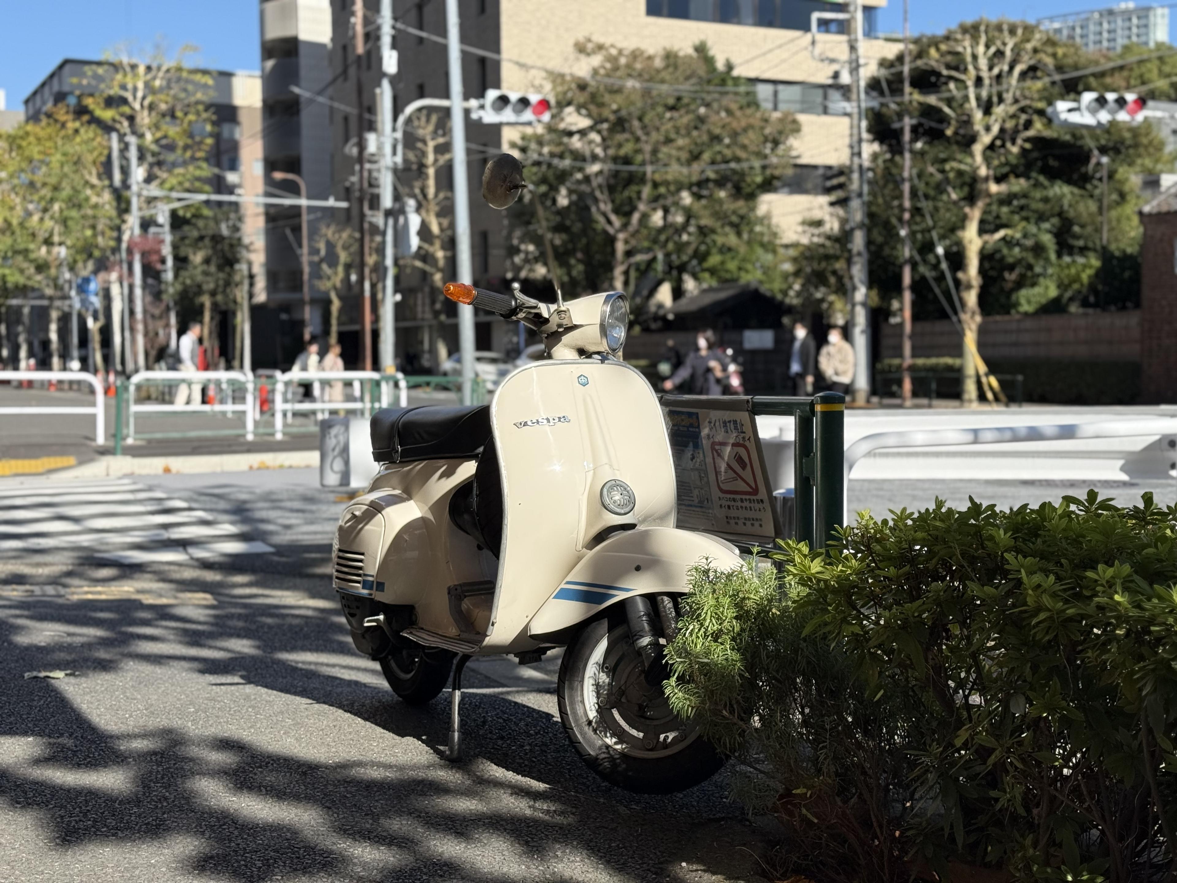 A cream-colored Vespa parked on a street corner in Tokyo